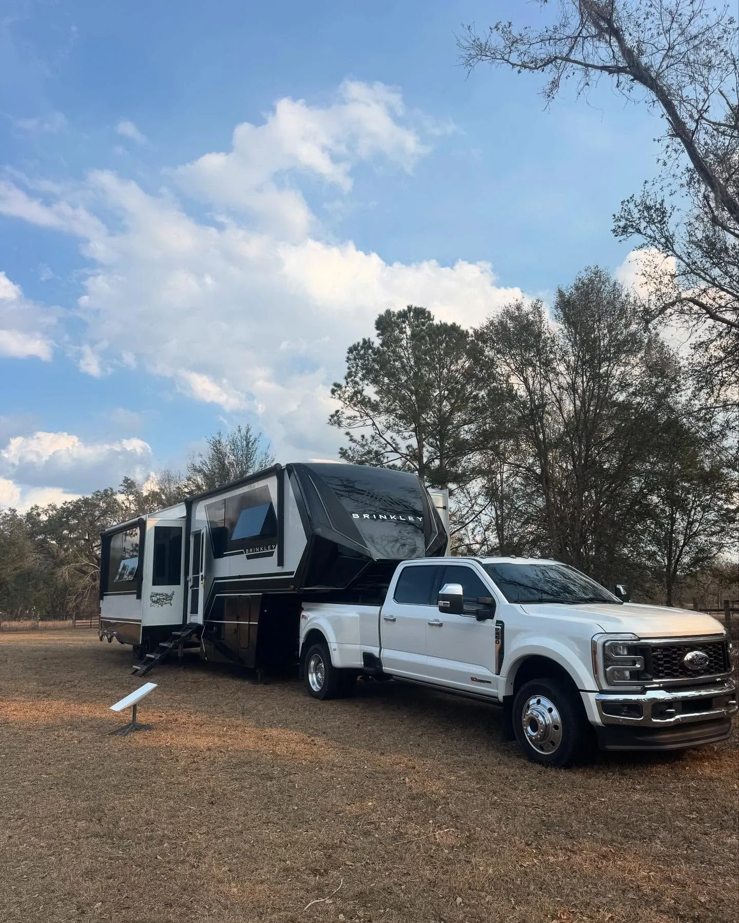 White Ford truck hitched to Brinkley RV parked in open campground setting.